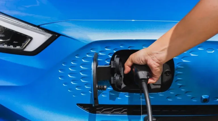 Devant d'un voiture électrique bleue avec main qui la branche à la borne de recharge